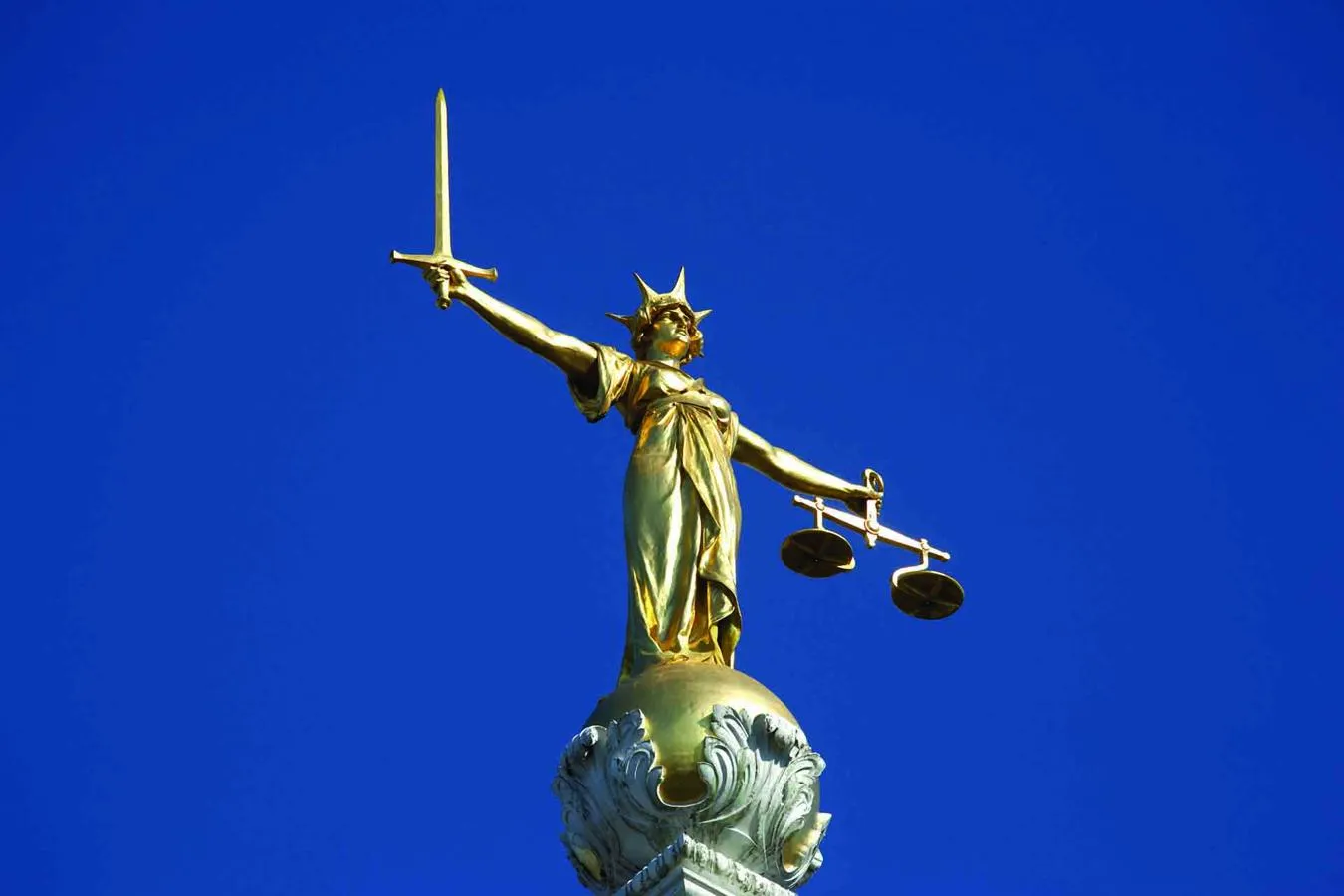 Bronze Statue of Justice holding sword and scales set against backdrop of bright blue sky