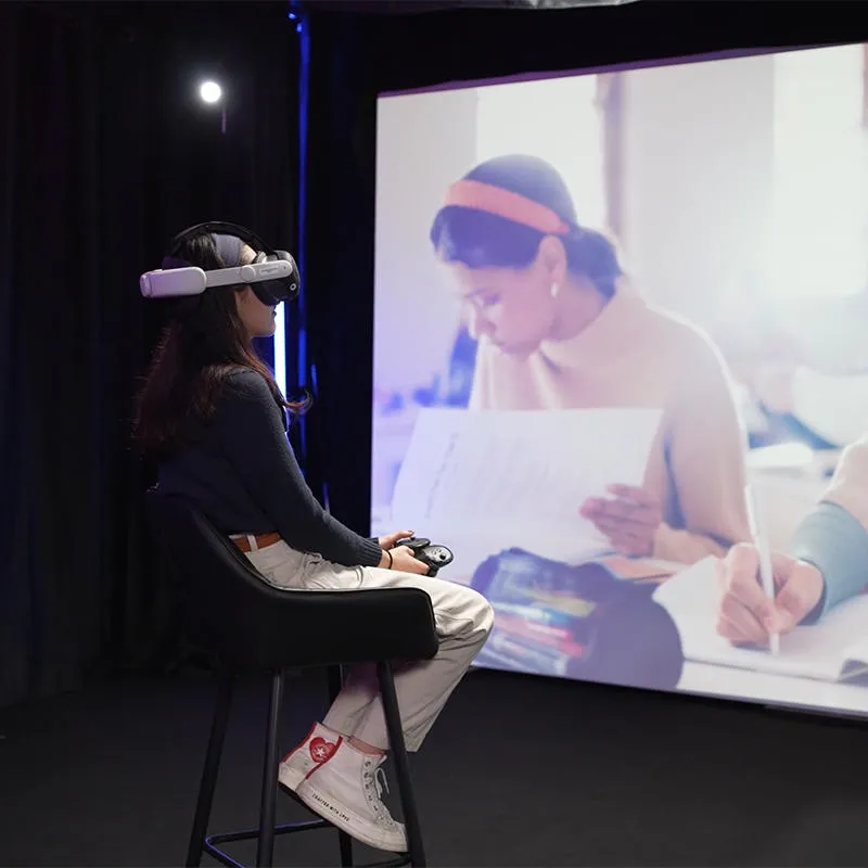 A student wears a VR headset in front of a large screen