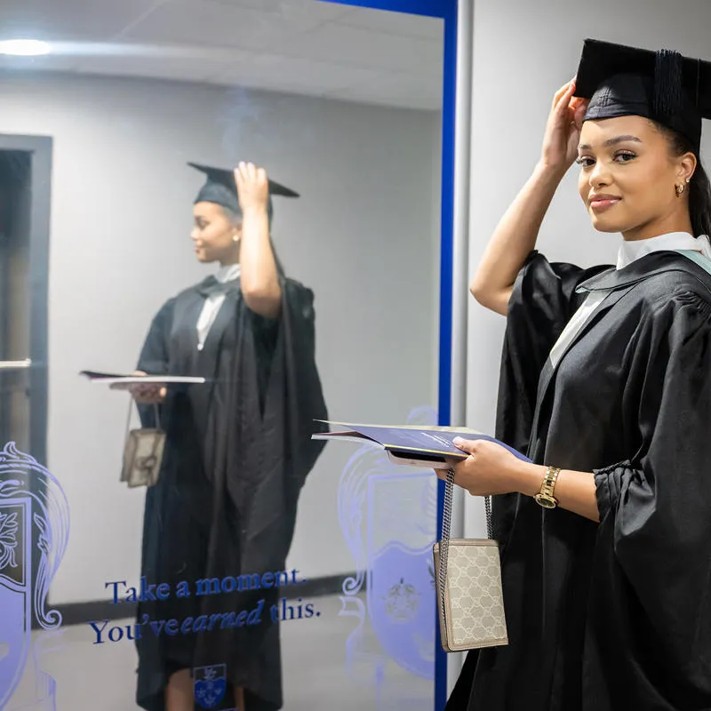 Student wearing graduation robes looking at the mirror