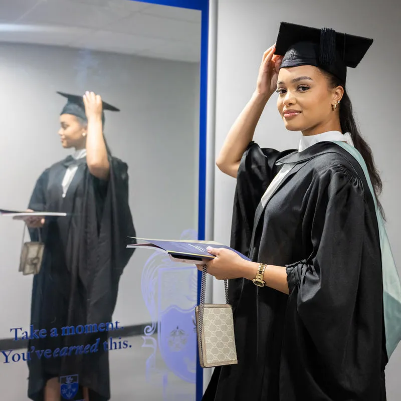 Student wearing graduation robes looking at the mirror