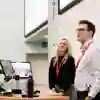 Woman and a man stood at the front of a lecture theatre with screens behind