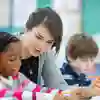 A female student teacher leans over the shoulder of a primary school child working at a desk