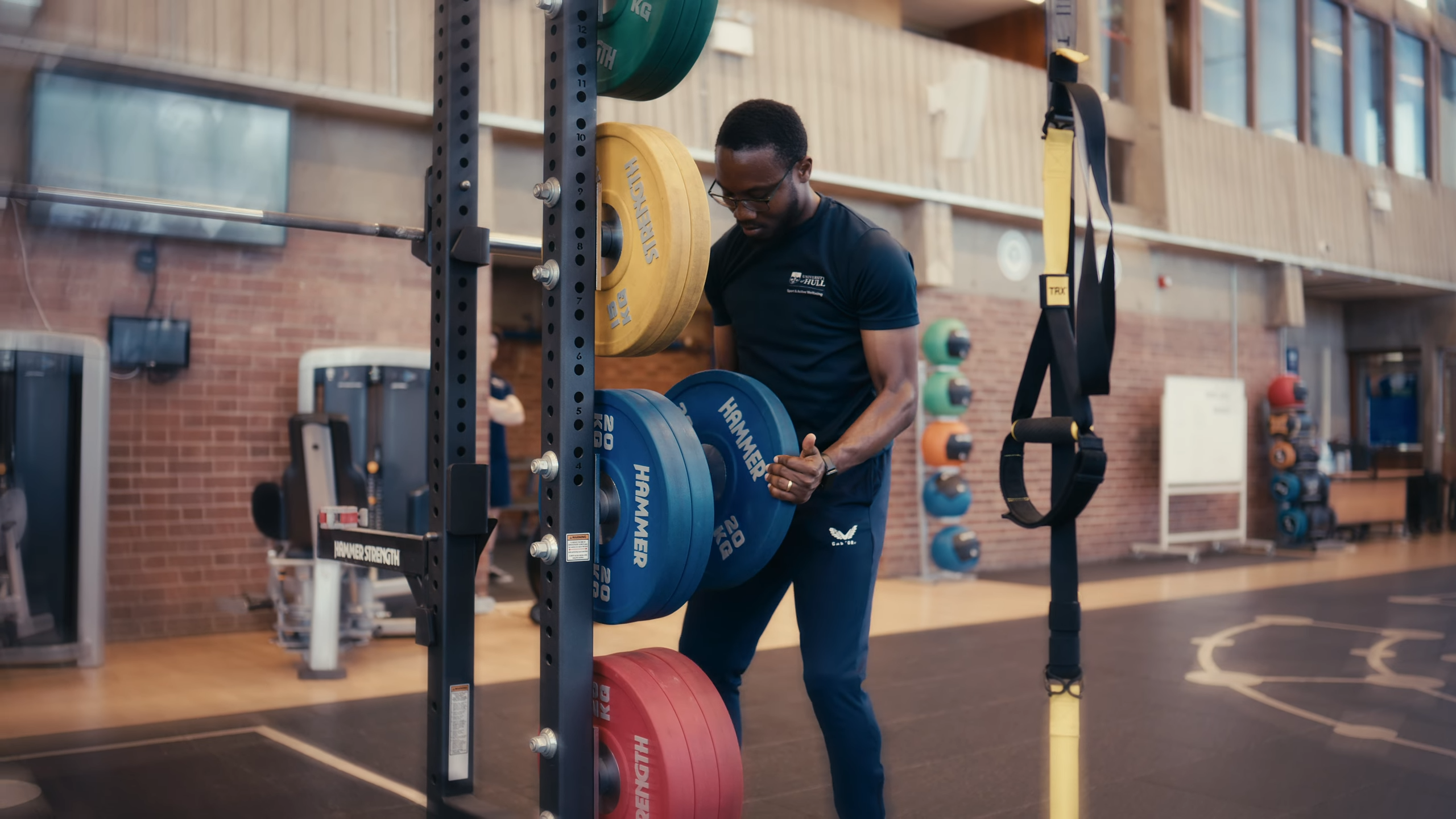 Temitope loading weight plates onto a barbell in a gym on campus at the University of Hull