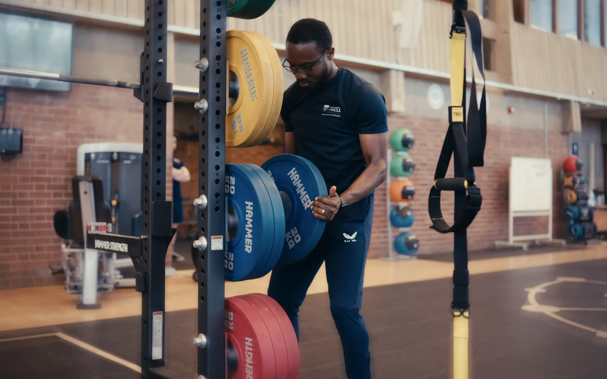 Temitope loading weight plates onto a barbell in a gym on campus at the University of Hull