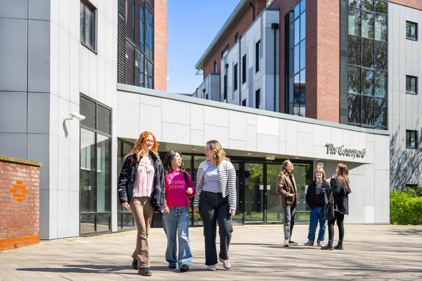 Two groups of students stand outside the entrance to The Courtyard accommodation on a bright, sunny day