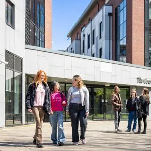 Two groups of students stand outside the entrance to The Courtyard accommodation on a bright, sunny day