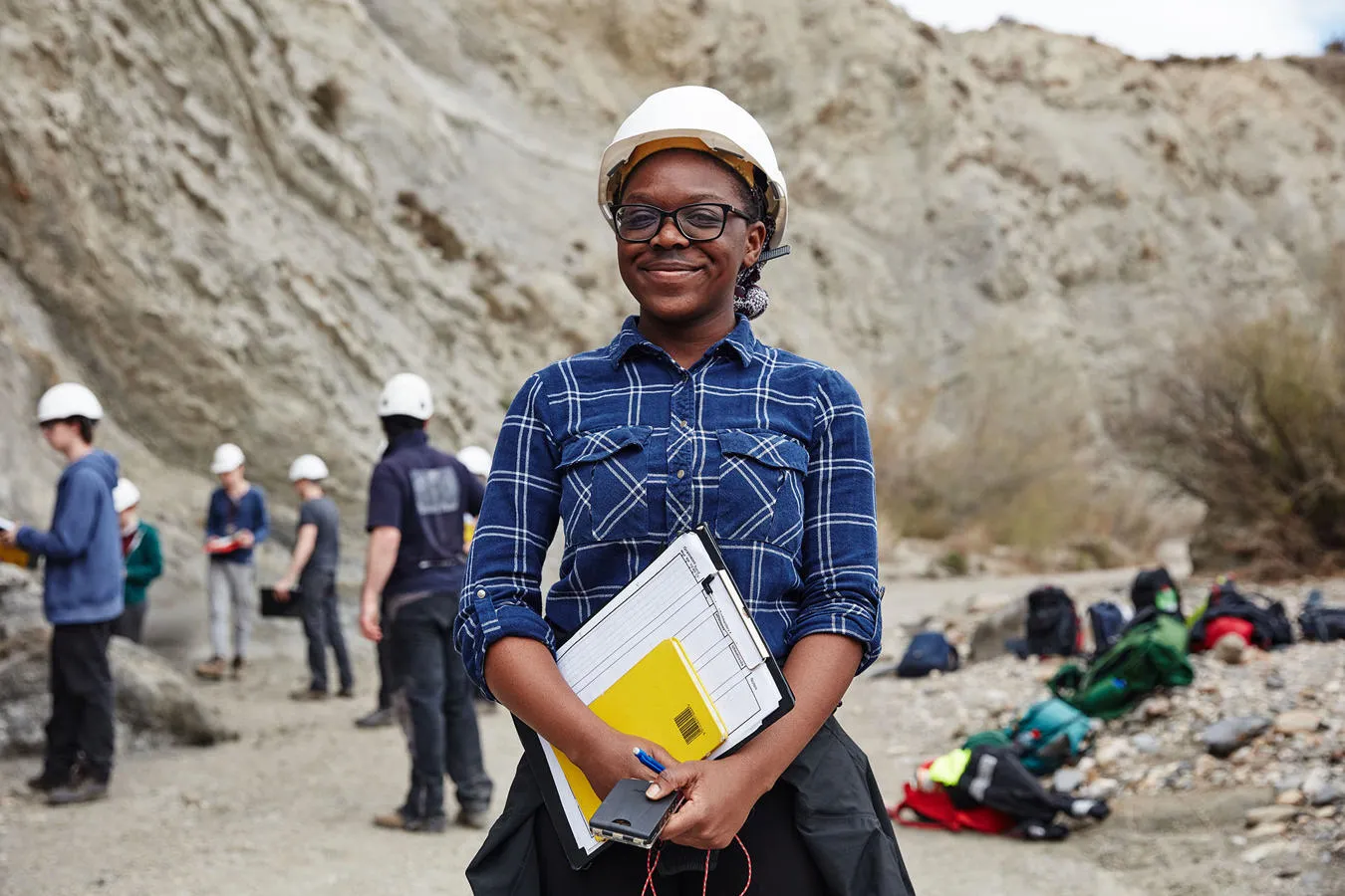 Smiling student wearing a hard hat and holding a clipboard 