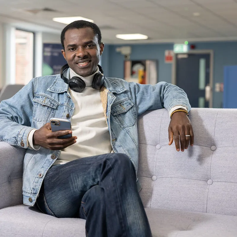 A business marketing student relaxes on a sofa with a mobile phone in his hand
