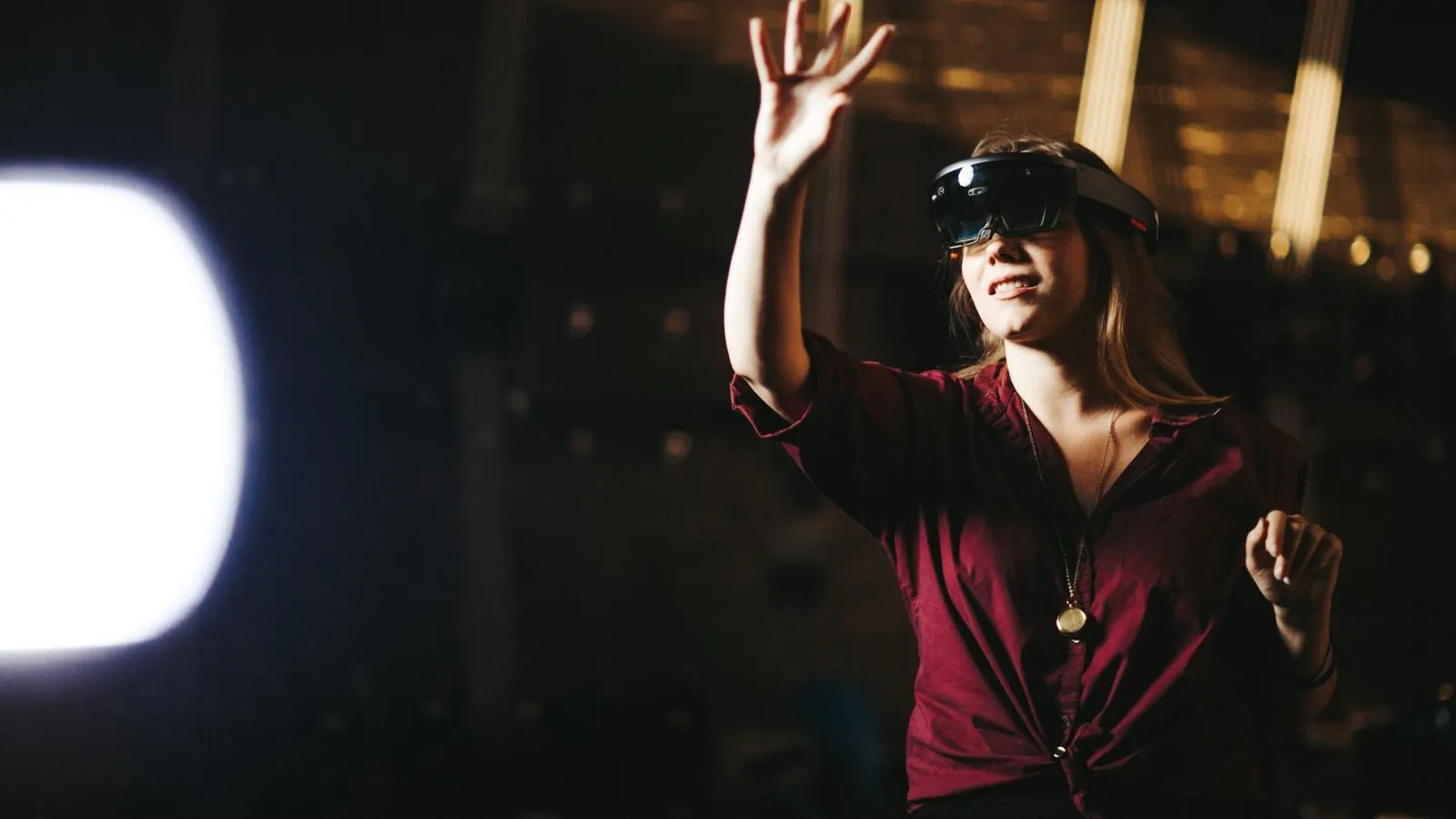 A female student wearing a Virtual Reality headset holds out her hand as if touching an object in the air