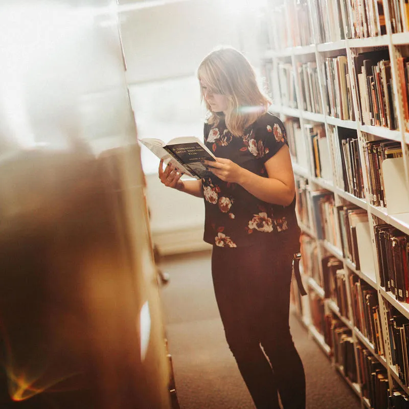 A student standing between the shelves in a library reading a book