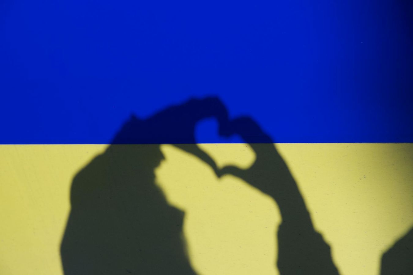 The shadow of two hands making a love heart sign overlay the colours of the Ukraine flag 