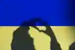 The shadow of two hands making a love heart sign overlay the colours of the Ukraine flag