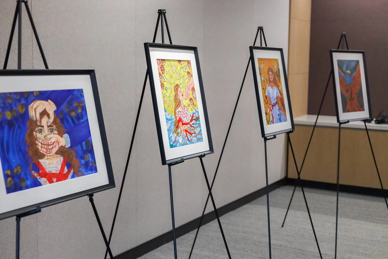 Four framed paintings created by modern slavery survivors, displayed on easels