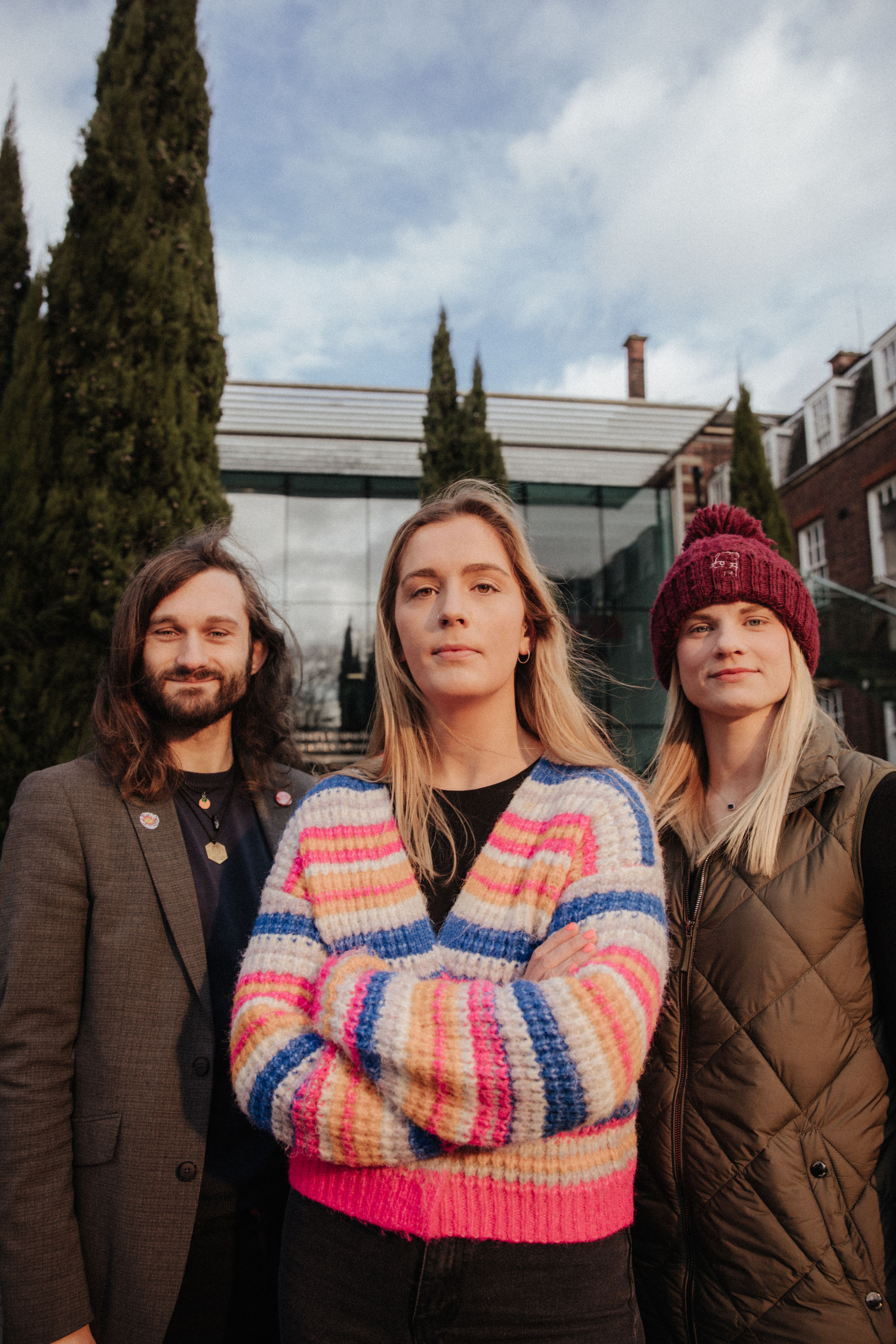 Three staff members stand confidently in front of the Business School