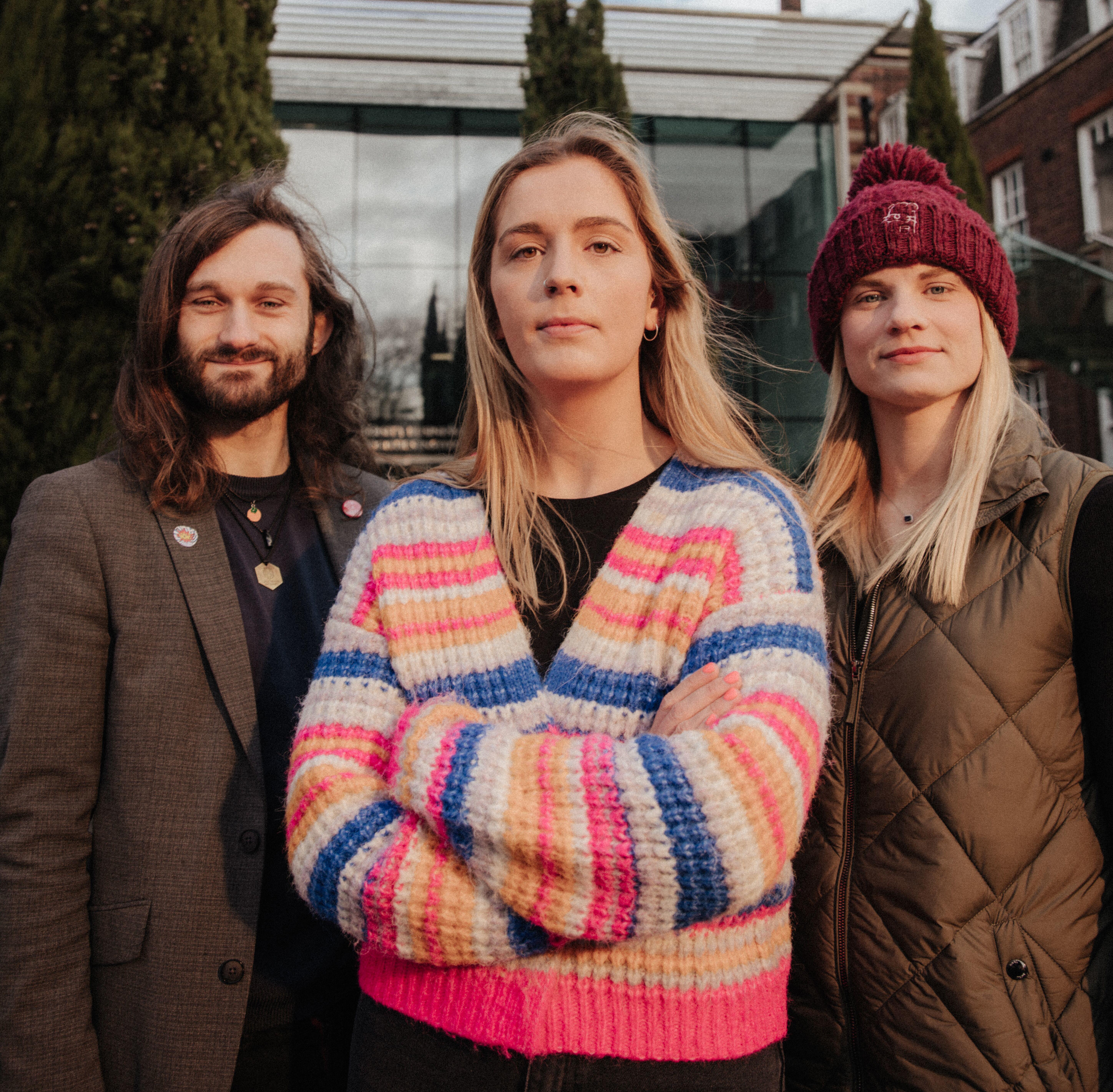 Three staff members stand confidently in front of the Business School