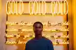 A student stands in front of gold illuminated neon writing, part of an artwork in Ferens Art Gallery