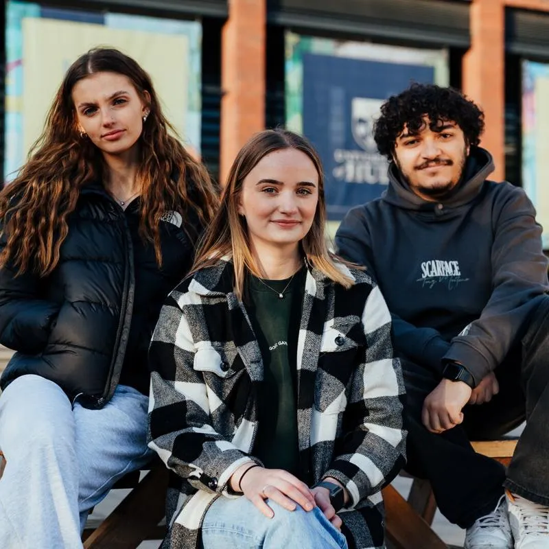 3 students looking to camera in front of university library