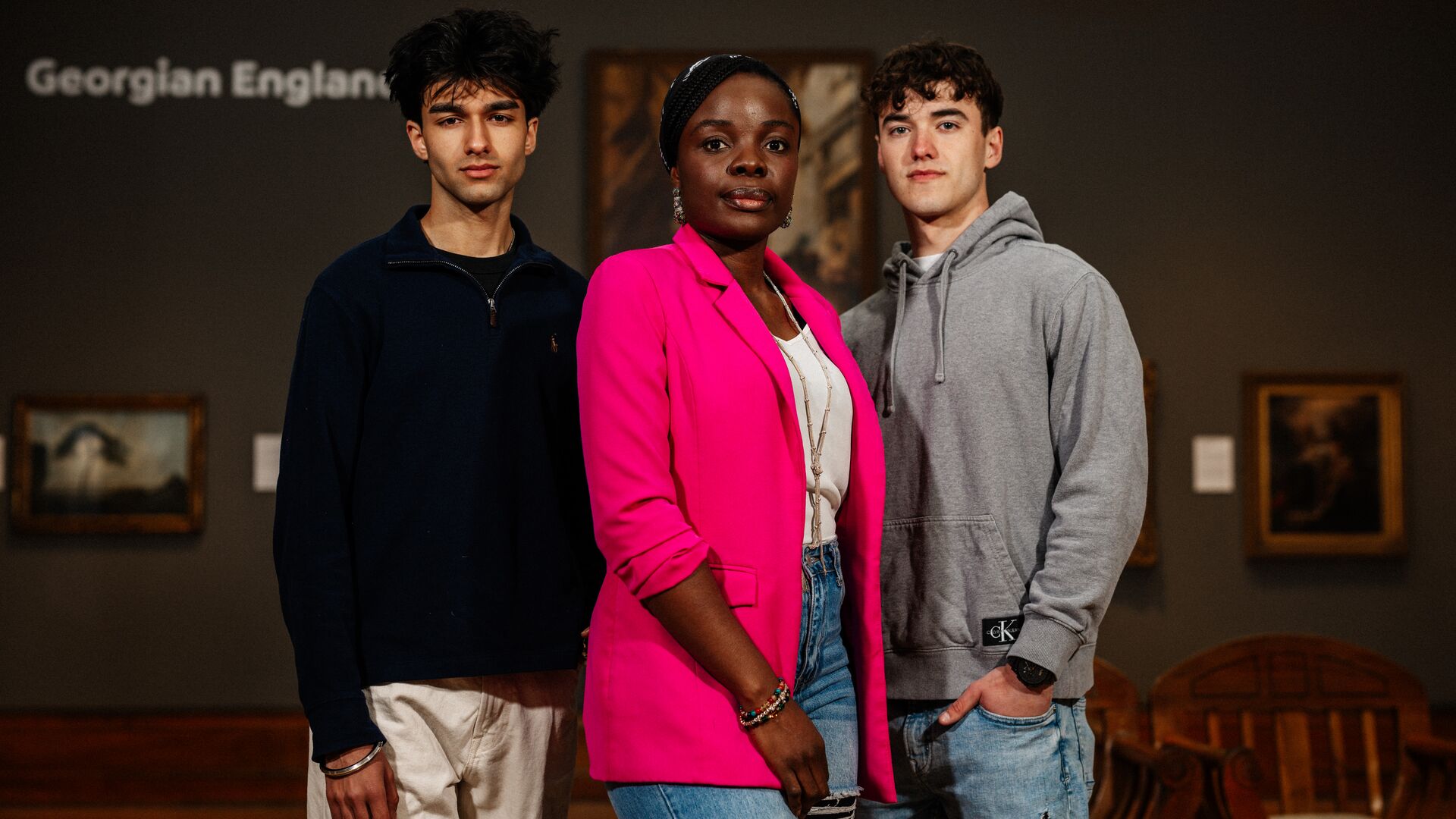 Three students stood in front of hung paintings at an art gallery