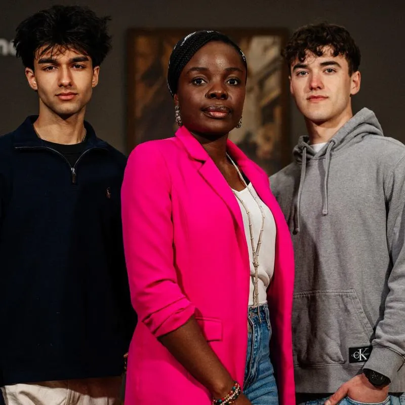 Three students stood in front of hung paintings at an art gallery