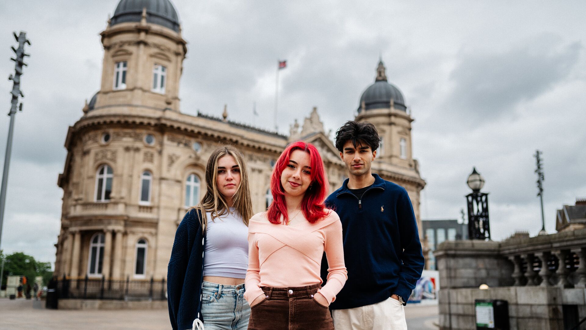 Three students dressed casually looking into the camera while standing in front of a large historical building