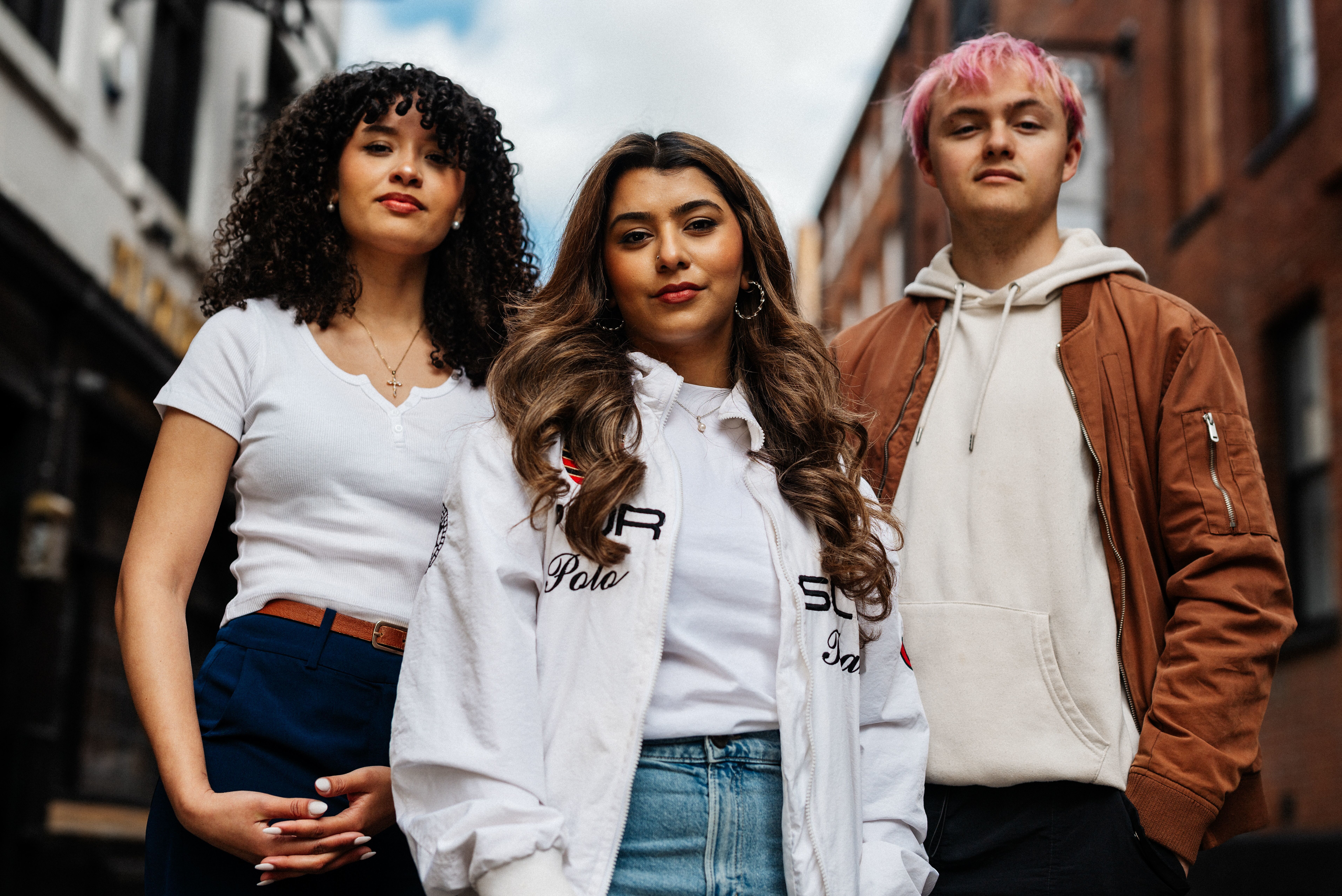 Three students stand confidently in front of old brick buildings in Hull's Old Town.