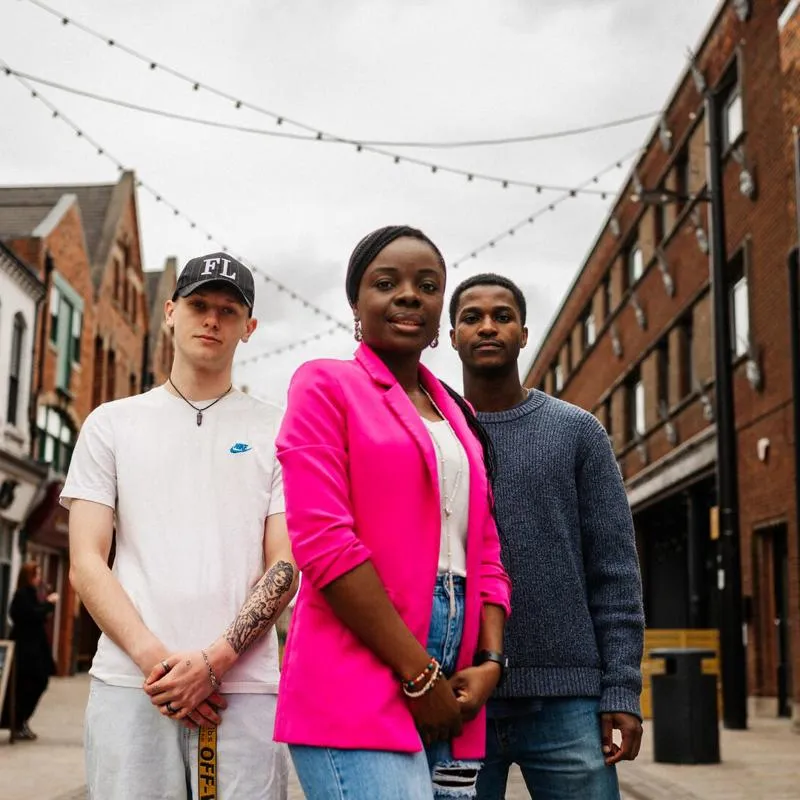 Three young adults standing in Humber Street, Hull, framed by brick walls and urban elements.