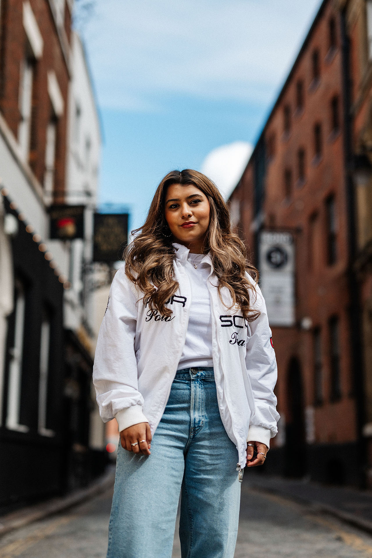 A casually dressed young woman stands in a cobbled street with old buildings either side.