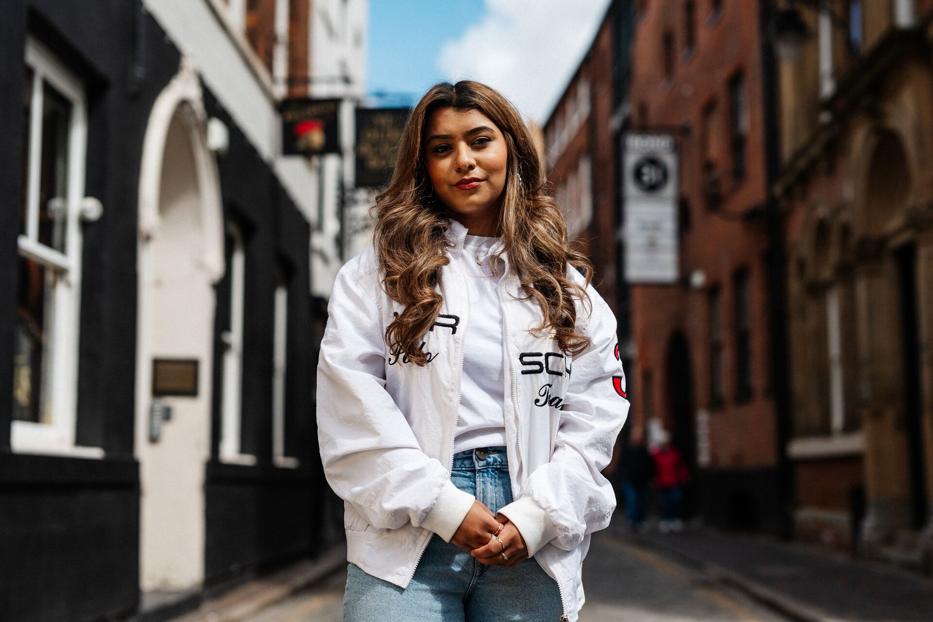 A female student stands smiling on a cobbled street in Hull's Old Town in front of historic pubs and other buildings