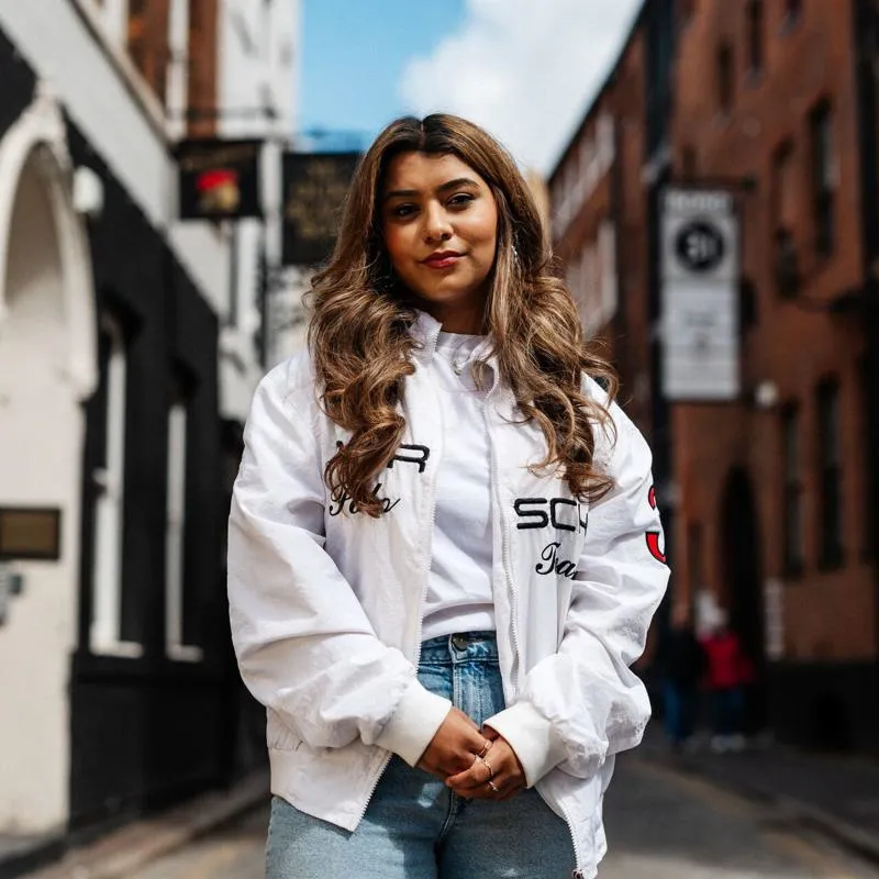 A female student stands smiling on a cobbled street in Hull's Old Town in front of historic pubs and other buildings