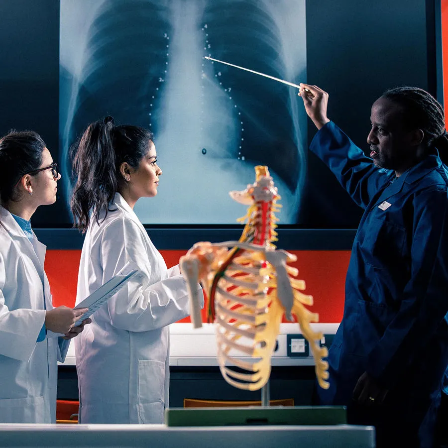 An instructor points to an x-ray image while three students in lab coats look on