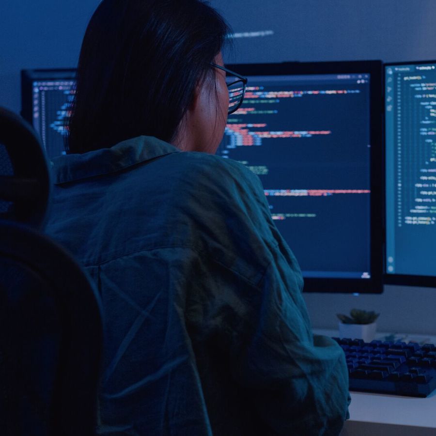 Woman looking at code on dual desktop screens in a dark room