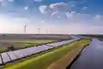 Wind turbines and solar panels in fields next to a river. 