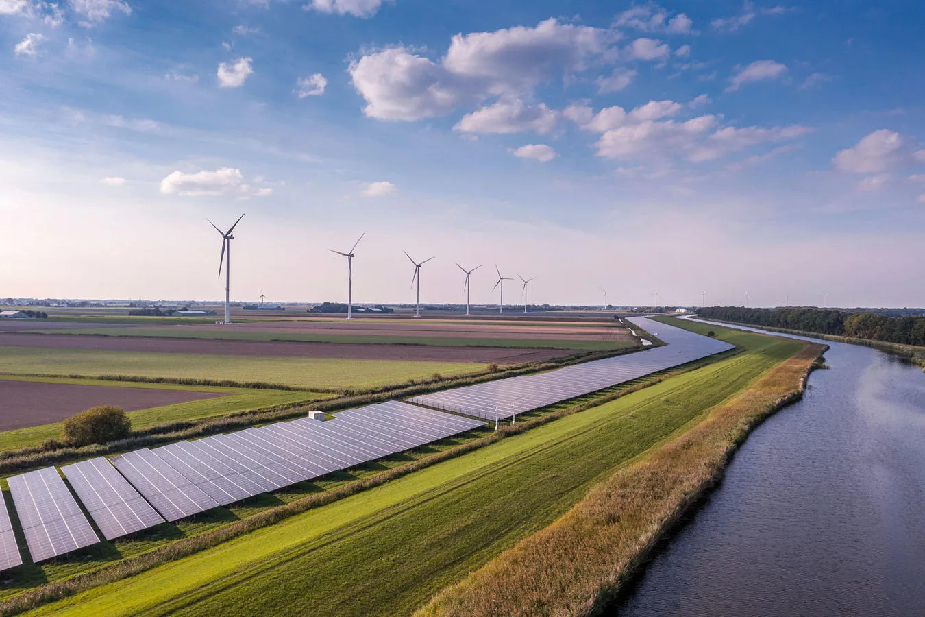 Wind turbines and solar panels in fields next to a river. 