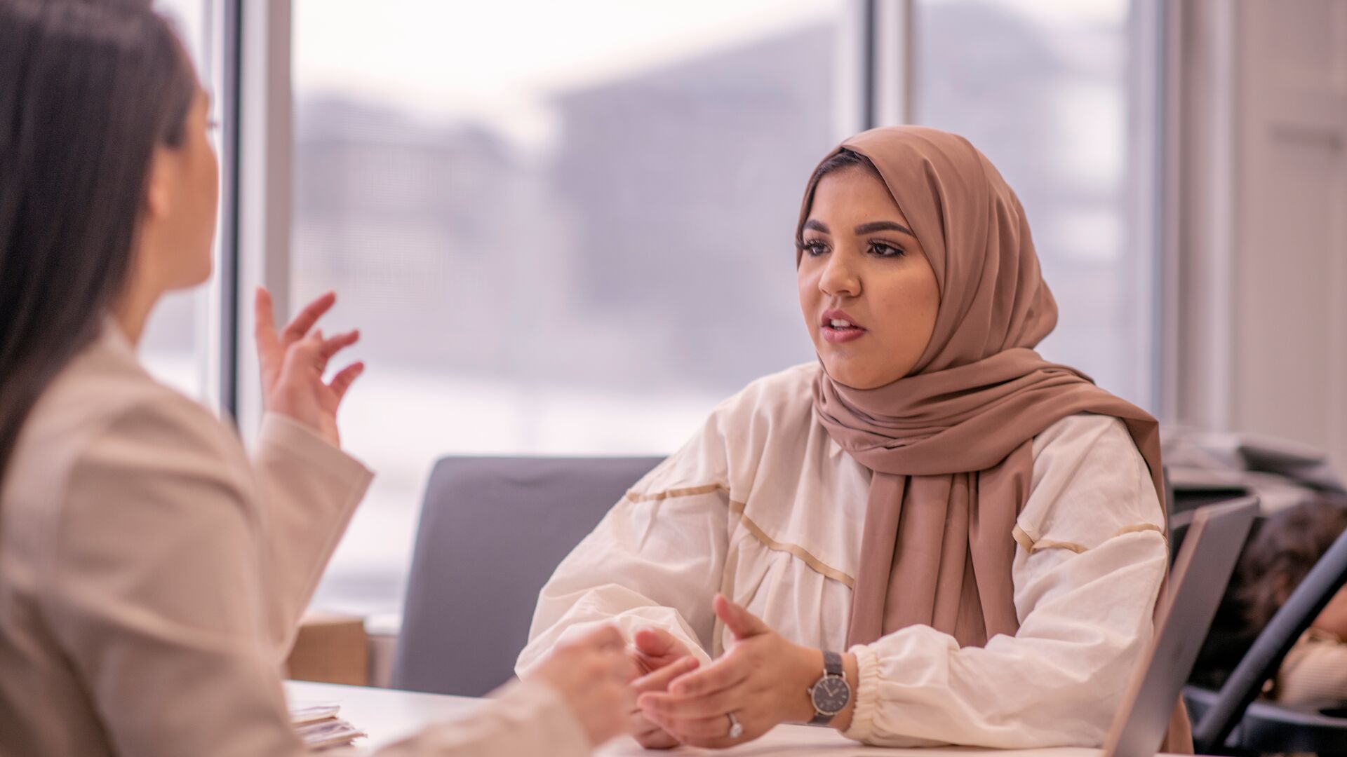a female student in a headscarf talking to an out of shot lecturer across a table