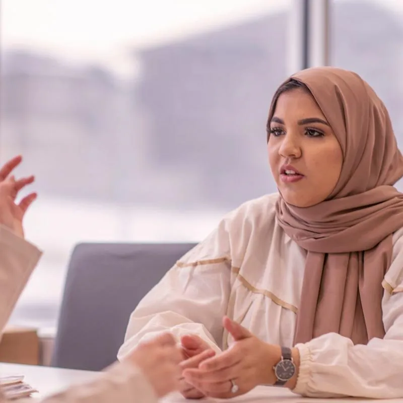 a female student in a headscarf talking to an out of shot lecturer across a table