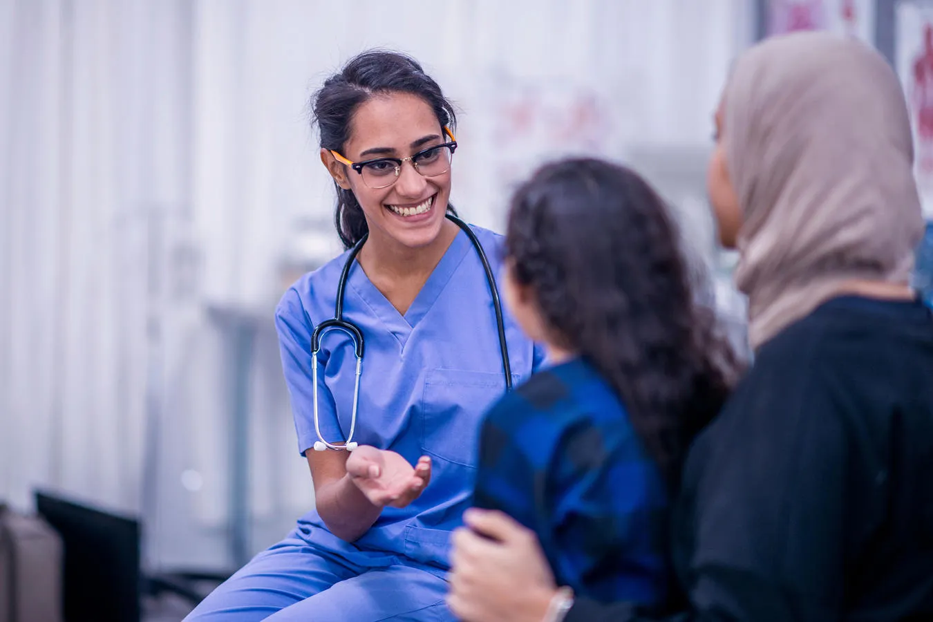 A female doctor in blue scrubs talking to mother and her child in a hospital ward