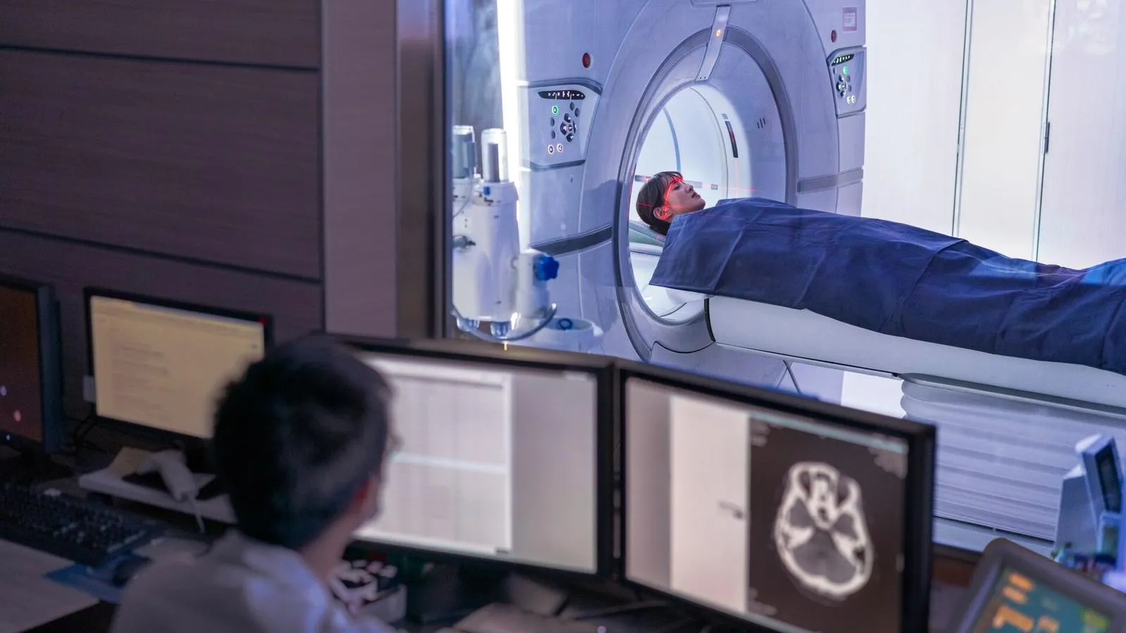 Doctor examining scan on computer while patient is entering into MRI scanner.