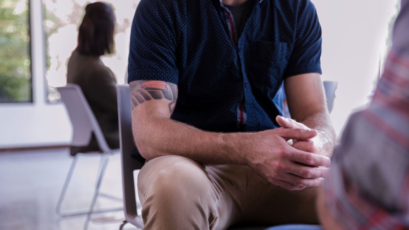 Man in dark blue teeshirt in a counselling session seen from shoulders down so face not seen.