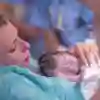 Mother holding new born baby that has been recently delivered by medical staff