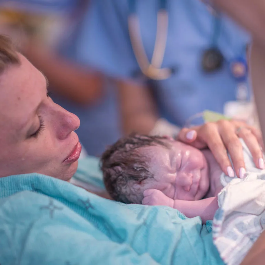 Mother holding new born baby that has been recently delivered by medical staff
