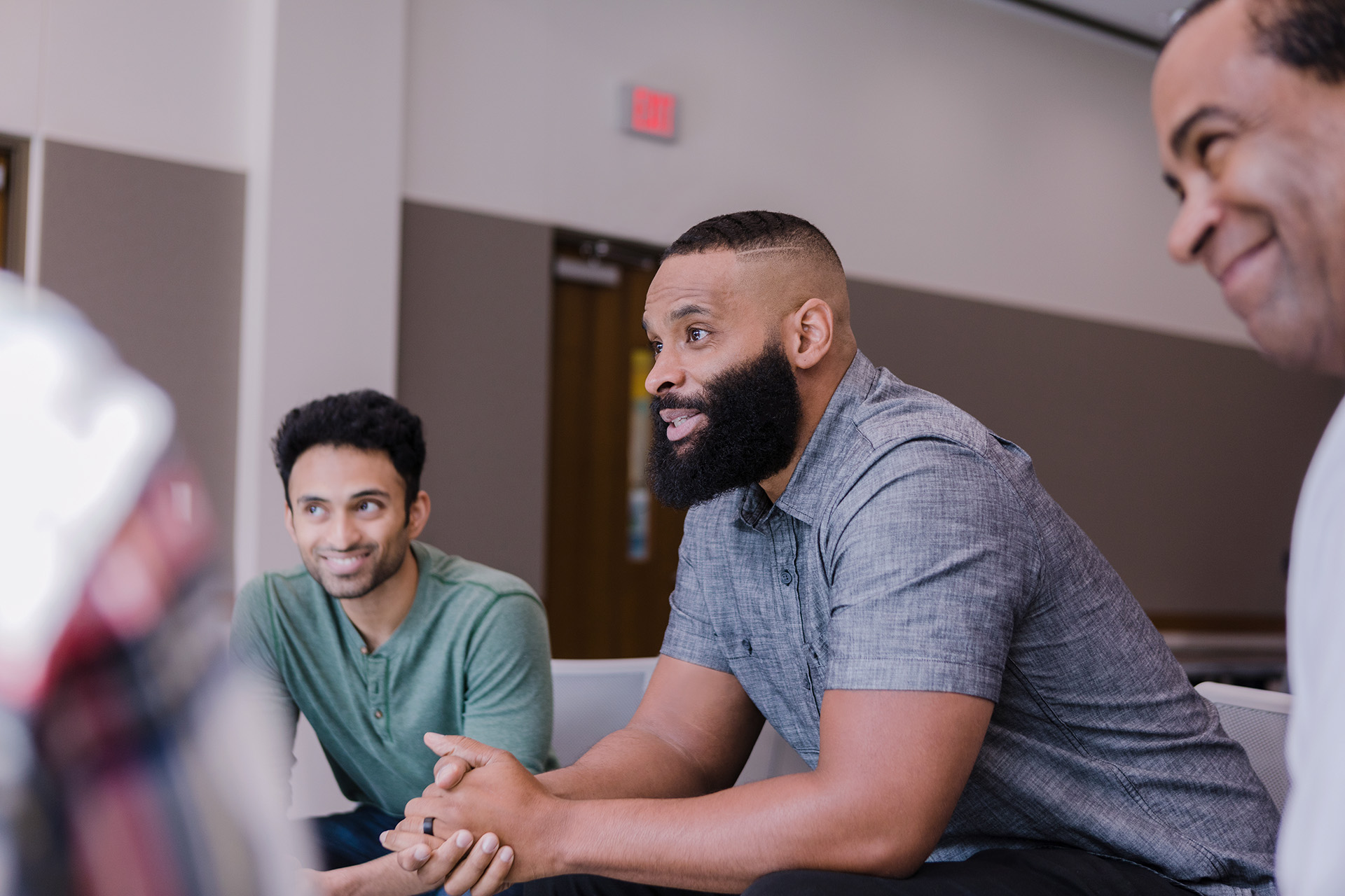 Three men seated around a conference table engaged in discussion in a meeting room.