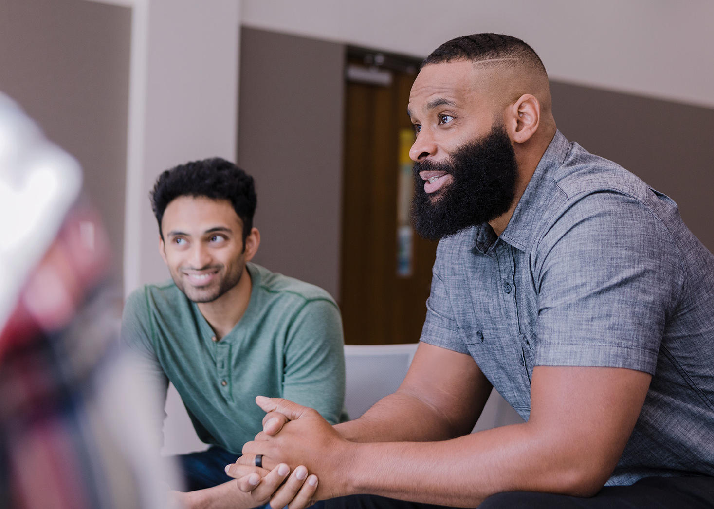 Three men seated around a conference table engaged in discussion in a meeting room.