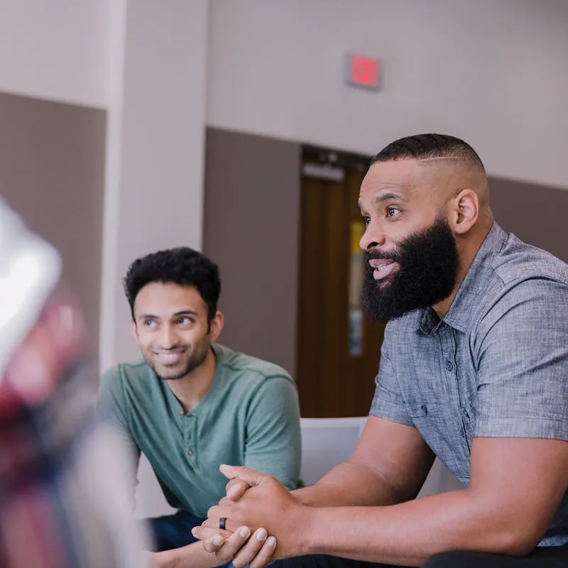 Three men seated around a conference table engaged in discussion in a meeting room.