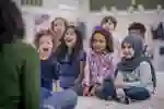 Happy young children sitting on the ground facing their teacher