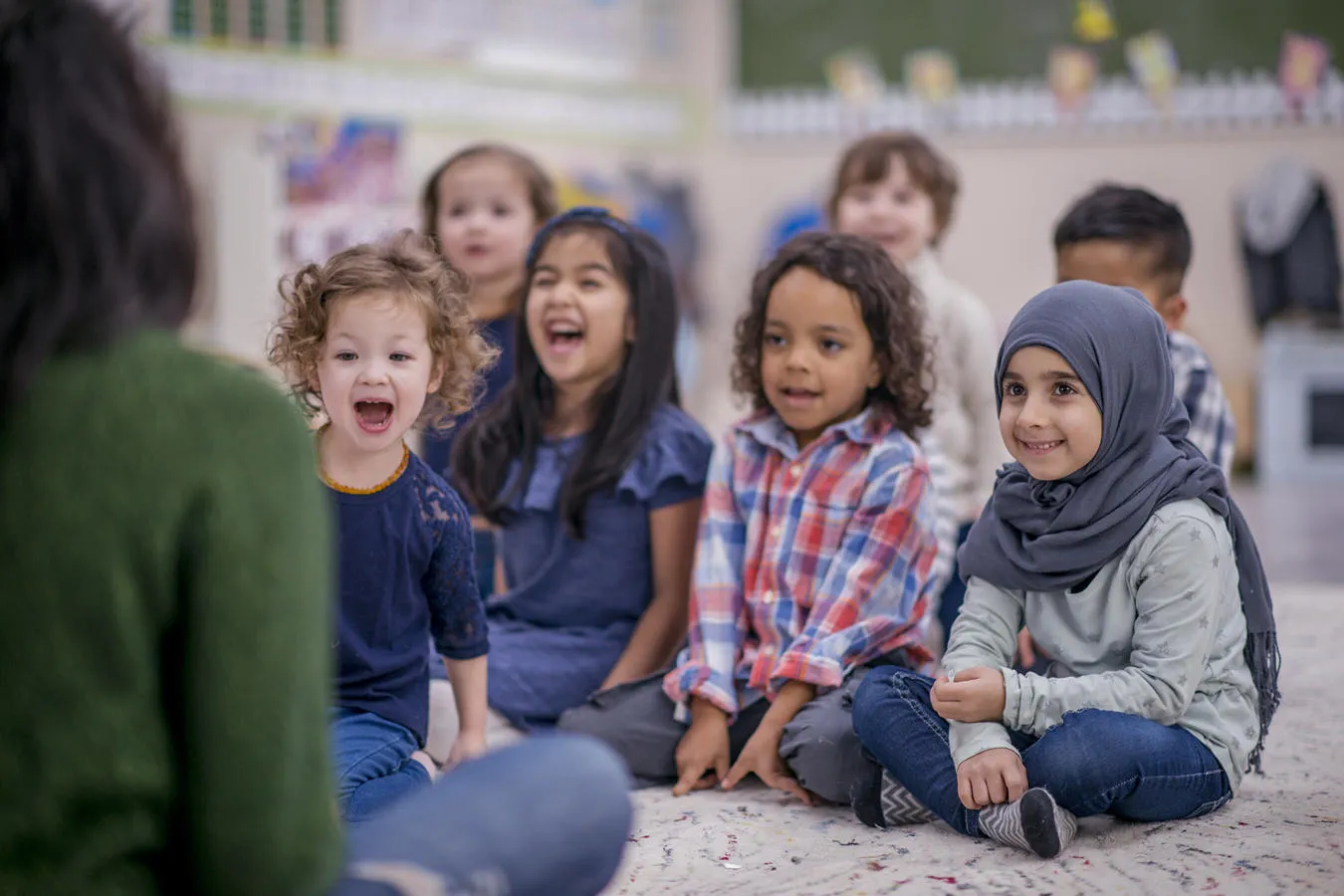 Happy young children sitting on the ground facing their teacher