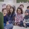 Happy young children sitting on the ground facing their teacher