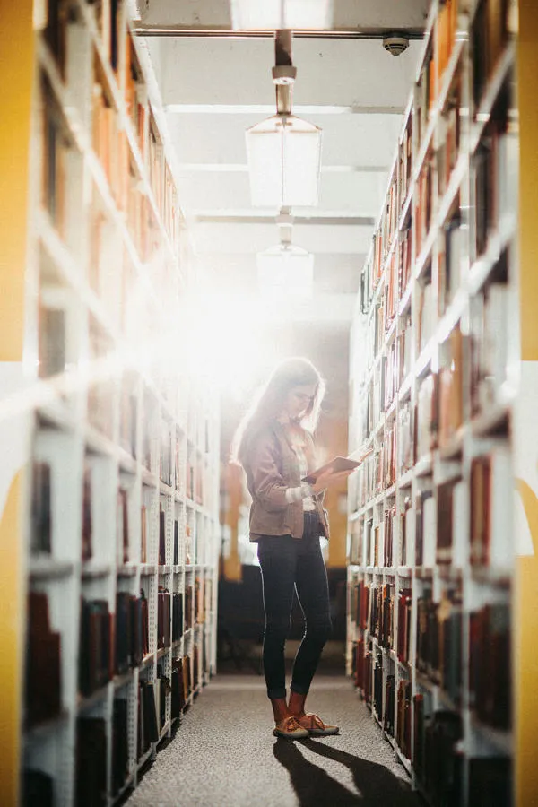 A students reads a book in front of library shelves