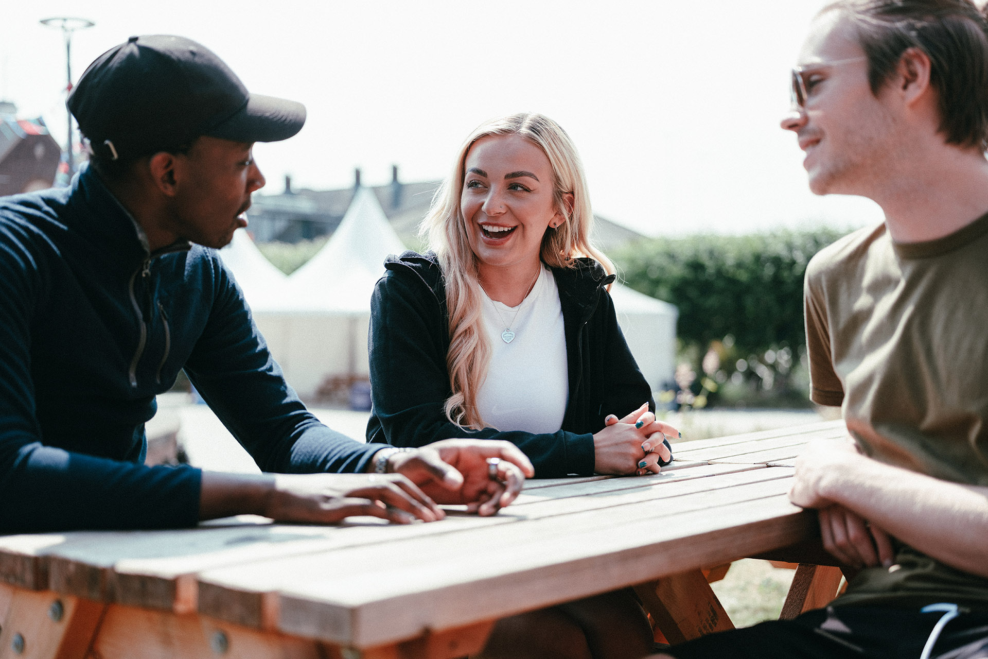 Three students sat on a bench on a sunny day.