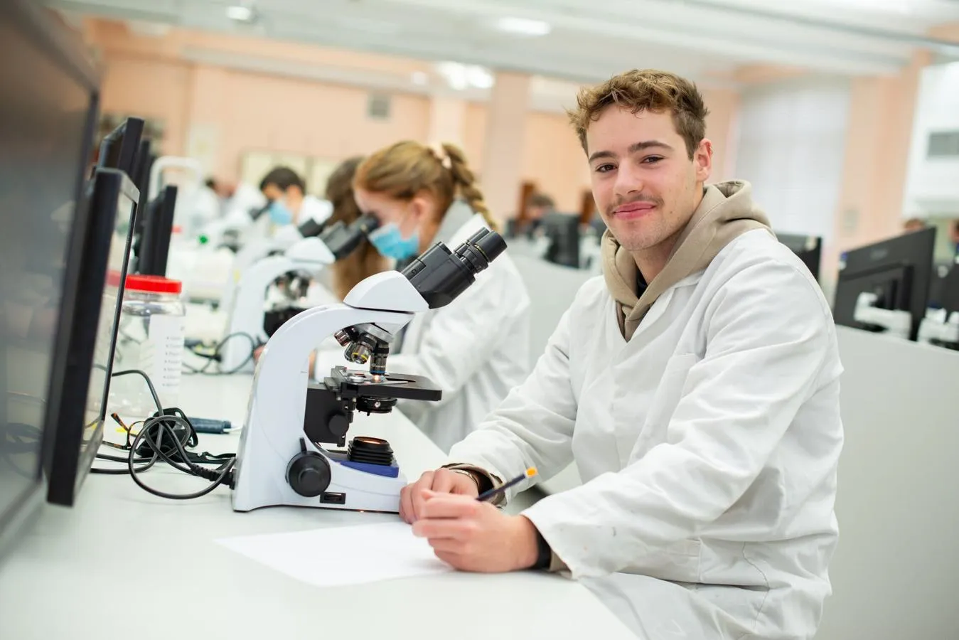 A student smiling whilst using a microscope.