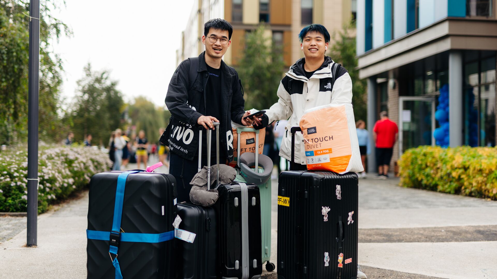2 international male students stood outside Westfield Court with suitcases on moving in day